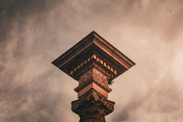 Low angle shot of a decorative stone column capital under a dramatic sky. © PapitasDark