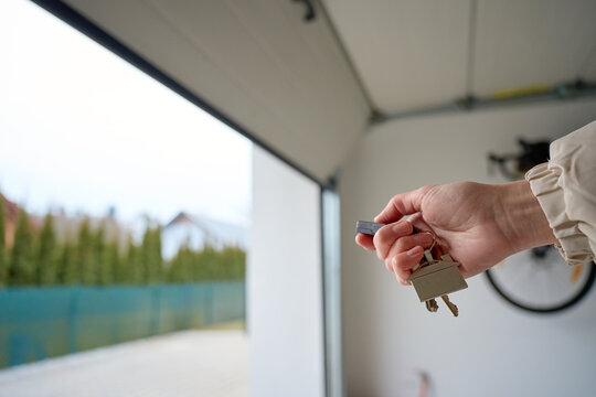 Closeup of hand holding garage remote and keys inside garage with open door