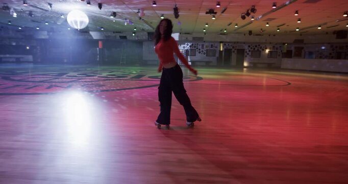 Cinematic shot of young woman doing awesome backwards skating tricks while alone on colorful disco floor