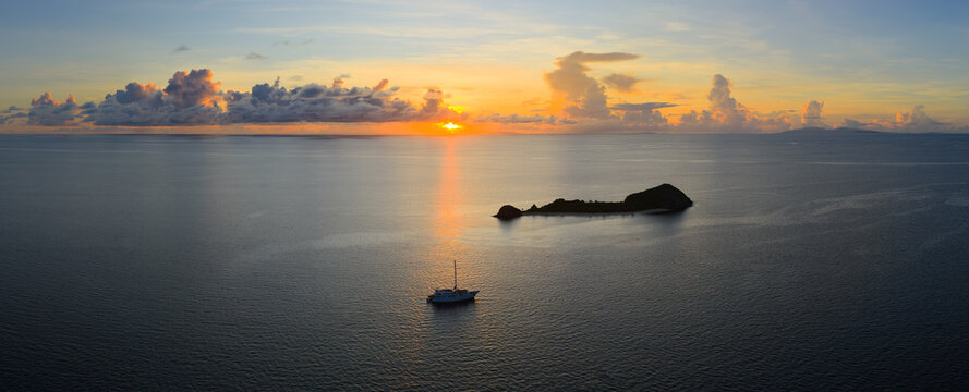 A serene sunrise silhouettes a small island in the Vatu-i-ra seascape in Fiji. This area is a marine protected area known for its high biodiversity and is a destination for divers and snorkelers.