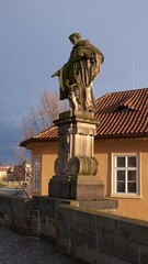 Fototapeta premium Statue on Charles Bridge standing on historic balustrade overlooking Prague rooftops