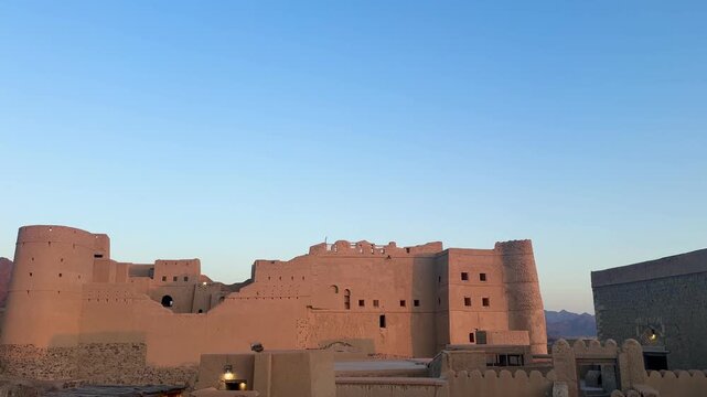 Historic Bahla Fort built with traditional mud architecture standing on rocky ground under clear blue sky showing ancient Omani heritage. Bahla, Oman - February 17 2026