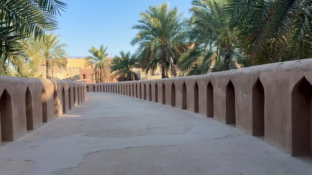 Historic Al Aqr Wall in Nizwa showing traditional Omani architecture with mud buildings palm trees and old defensive structure in a famous cultural landmark. Nizwa, Oman - February 20, 2026