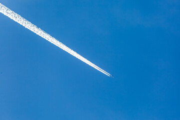 High altitude passenger jet flying in clear blue sky with long white contrails. © J.Woolley