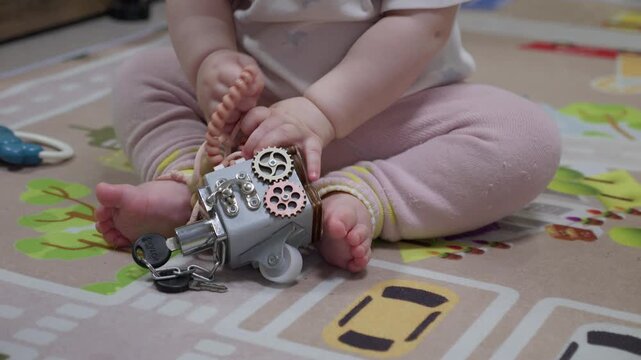 A baby holds various toys, including a puzzle box and turtle on a patterned rug. Concept of early childhood development and sensory play for infants. 