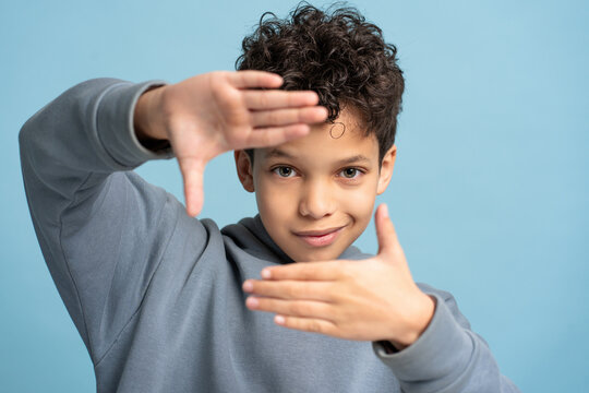 Smiling handsome little boy showing frame with hands looking at camera isolated on blue background