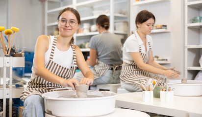 During master class, two young women and teen girl works with clay blank, processes with potter...