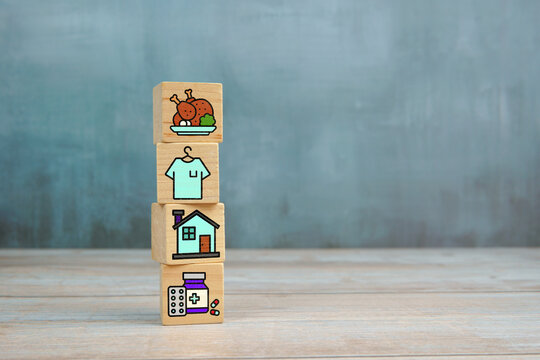 Basic human needs concept with wooden blocks showing icons of food, clothing, housing and medicine on wooden table.