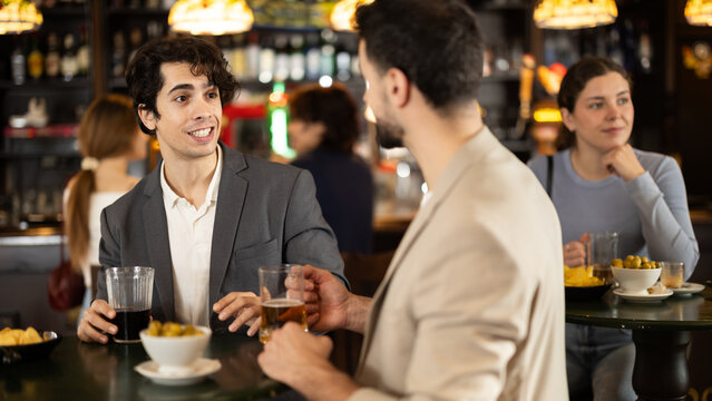 Young men come to the bar after work, drinking beer with snacks and chatting about everyday activities. Friends drinking drinks in sports bar