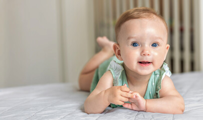 Fototapeta premium Smiling baby lying on bed with copyspace