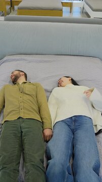 Happy couple holding hands falling backwards onto bed