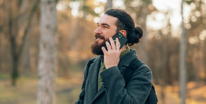 Bearded Man talking on smartphone in Autumn Park Wearing Wool Coat And Bun.