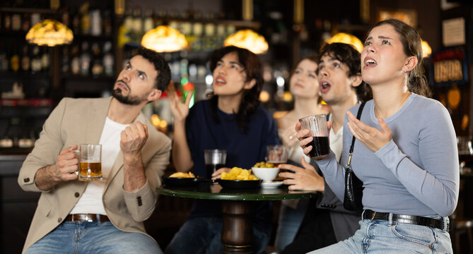 Sports fans react with disappointment to changes in bad luck game. Sports fans enjoy watching match broadcast at sports bar. Young people drink beer, stare at TV screen, and watch their idols play.