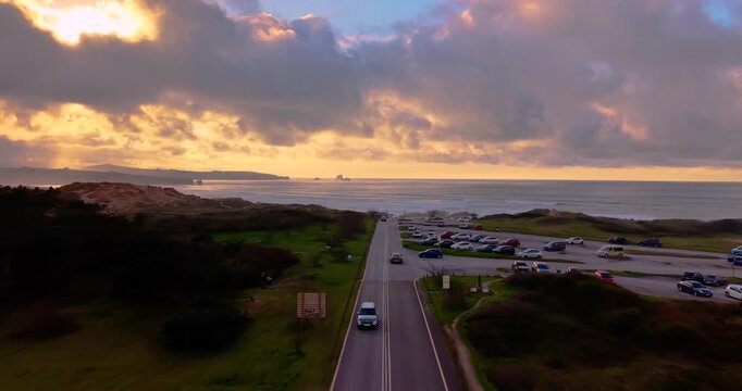 Panoramic aerial footage capturing a car driving along the scenic road to Valdearenas beach in the Liencres Dunes Natural Park. Awesome route close to the sea in a golden sunset in North of Spain.