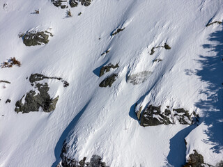 Aerial View of Snow-Covered Rocky Mountain Slope With Tree Shadows in BC, Canada