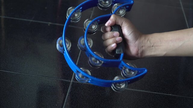 Hand Shaking Blue Tambourine with Metal Jingles Close-Up