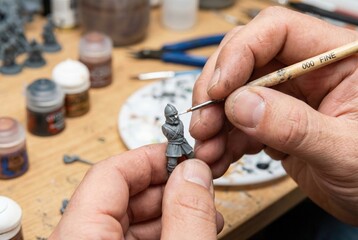 Hobbyist using a fine brush to carefully paint the eye of a grey plastic miniature figure