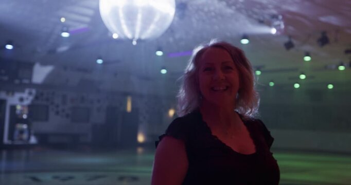 Blonde female skater doing fast, impressive spin move in front of disco ball - steady cam medium shot