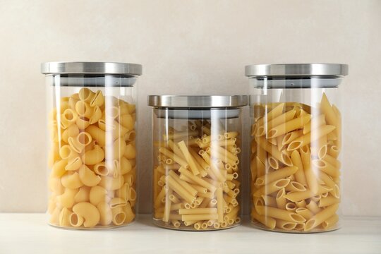 Different types of pasta in jars on white wooden table