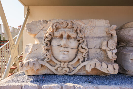 Ancient stone carving of a face with curly hair and decorative elements, Medusa Gorgon from Greek mythology