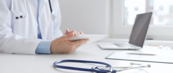 Closeup of blue stethoscope is lying on the table near female doctor reviewing prescription on...