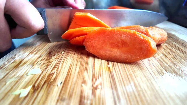 Bright orange carrots being expertly sliced with a sharp knife on a wood cutting board. Fresh vegetable preparation for a healthy meal