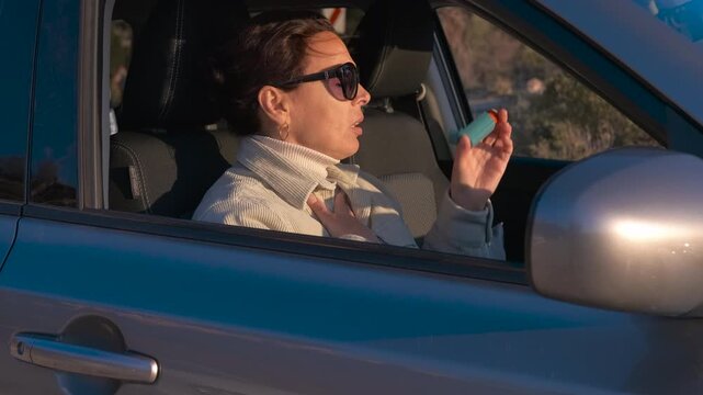 Asthmatic woman using an inhaler while driving her car dult woman with sunglasses experiencing an asthma attack and breathing difficulties while driving her car, using a medical inhaler