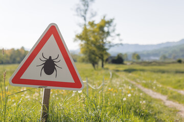 A sign warns of tick risks on a path in nature. Hikers should be aware of Lyme disease and...