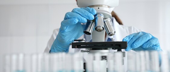 Female scientist wearing protective equipment checking microscope, analyzing blue test tubes in modern laboratory research setting. Medicine, healthcare and science concept © rogerphoto