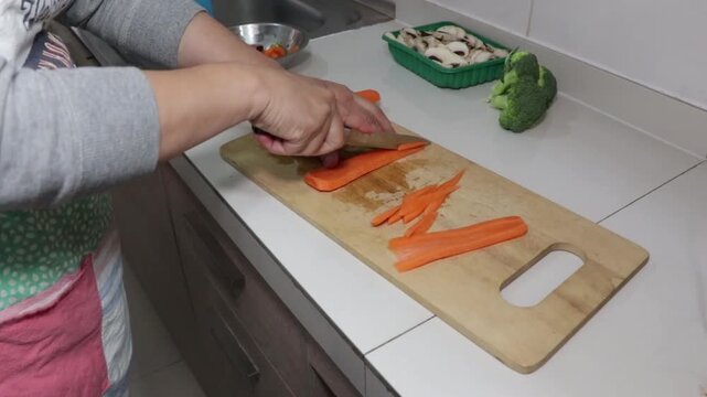 cortando zanahorias en juliana sobre una tabla de madera en la cocina