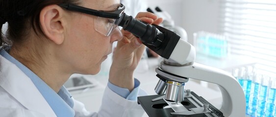 Female scientist examining microscope slide, analyzing research data in sterile laboratory...
