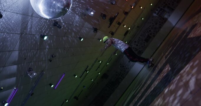 Stylistic tilt shot of professional, young skater doing crouching spin before falling