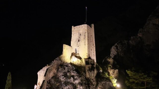Aerial drone perspective of Mirabela fortress illuminated above Omis town at night.