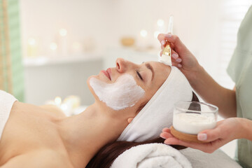Plakat Beautician applying moisturizing mask with brush onto woman's face indoors, closeup