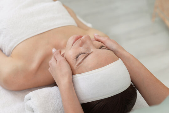 Beautiful woman in spa headband receiving facial massage on couch indoors, closeup