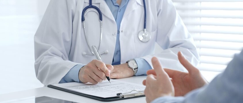 Female medical professional filling prescription, advising patient on health issues during clinical consultation. Medicine and healthcare concept
