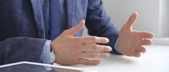 Businessman wearing blue suit and wristwatch, is sitting at white desk explaining business strategy...