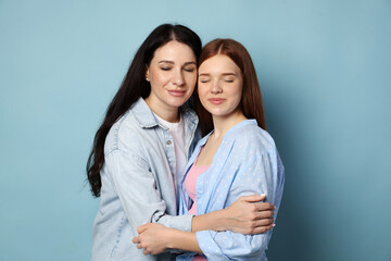 Mother and her teenage daughter hugging on light blue background