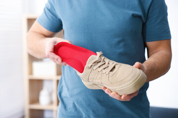 Man putting orthopedic insole into shoe indoors, closeup