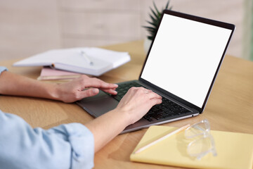 Woman typing on laptop at wooden table indoors, closeup