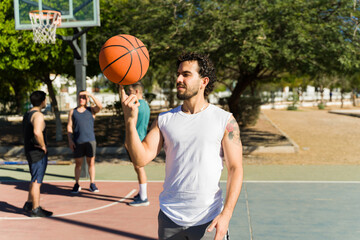 Naklejka premium Young sportsman spinning a basketball on his finger while practicing with friends on an outdoor court