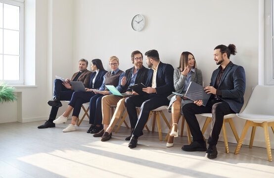 Applicants waiting for interview in lobby. Candidates chat and review resumes and laptops, sharing tips and preparing notes for hiring. Useful for business recruitment, team and career visuals.