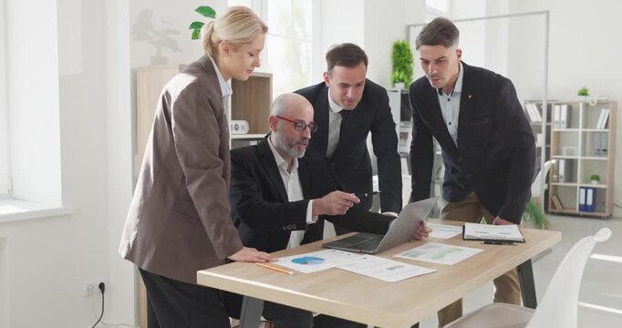 Business team meeting planning strategy in office. Colleagues gather around a laptop, reviewing charts and timelines with focused discussion. Clear concept of teamwork and partnership.