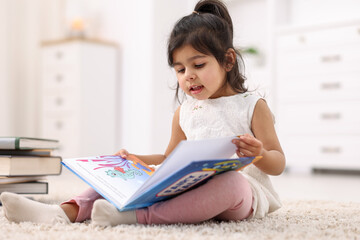 Naklejka premium Cute little girl reading book on floor at home