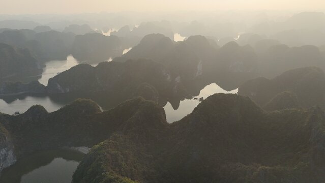 Beautiful sunrise over Ha Long Bay with limestone karst islands rising from the emerald water, traditional boats sailing between the cliffs in northern Vietnam.