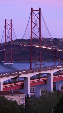 View of Lisbon view from Miradouro do Bairro do Alvito tourist viewpoint of Tagus river, traffic on 25th of April Bridge, and Christ the King statue in the evening twilight. Lisbon, Portugal