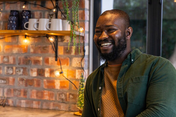 African American man smiling while sitting at counter in cafe wearing green shirt, ceramic mugs