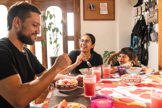 Father smiling while eating lunch at the dining table, sharing a relaxed family moment in a warm home environment. Smiling father enjoying lunch with family at home