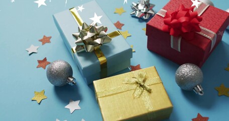 Displaying three wrapped gifts arranged on light-blue table, with silver baubles and star confetti