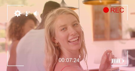 Smiling blonde woman facing camera at bar, red top, hoops, holding clear glass with straw, REC
